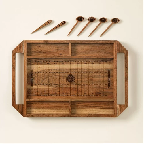 a cheese board made of wood in the shape and has details of a football field. ohio state logo in the middle of the field. cheese sticks off to the side look like footballs on top 