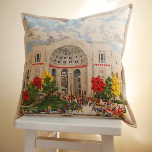 An Ohio State throw pillow featuring a detailed illustration of the Stadium Rotunda, resting on a white wooden stool.