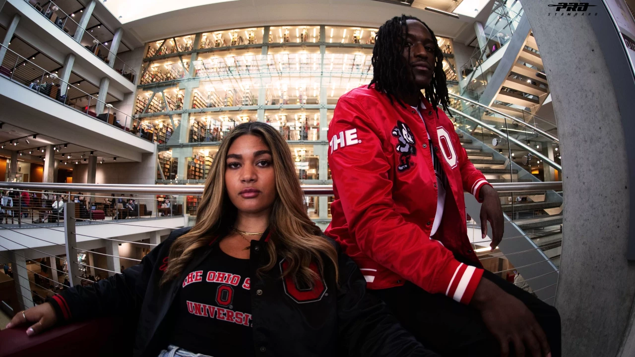 Two models sit side by side. The model on the left wears a black ohio State shirt and a jacket. The model on the right wears a red Ohio State jacket with a THE on the arm, and Brutus and the Block O on the chest. 